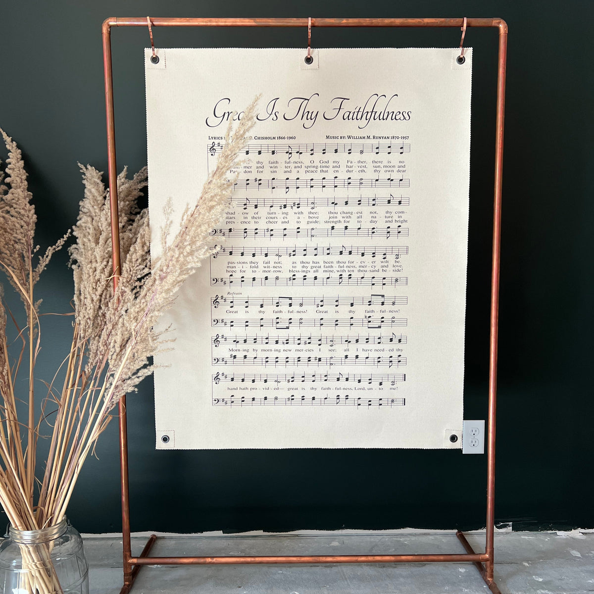 Sheet music on a metal stand against a dark wall with dried plants.