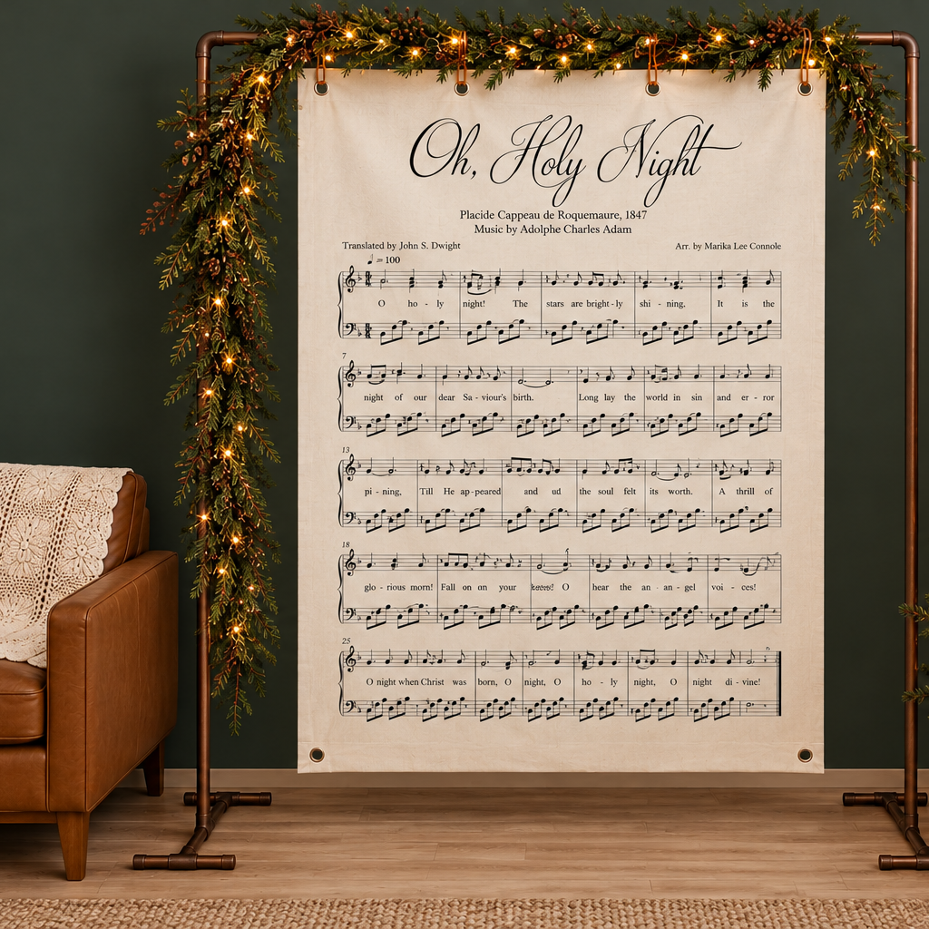 Oh Holy Night Christmas hymn wall canvas displayed on a copper frame with green garlands and warm white string lights, beside a brown leather armchair on a wood floor.
